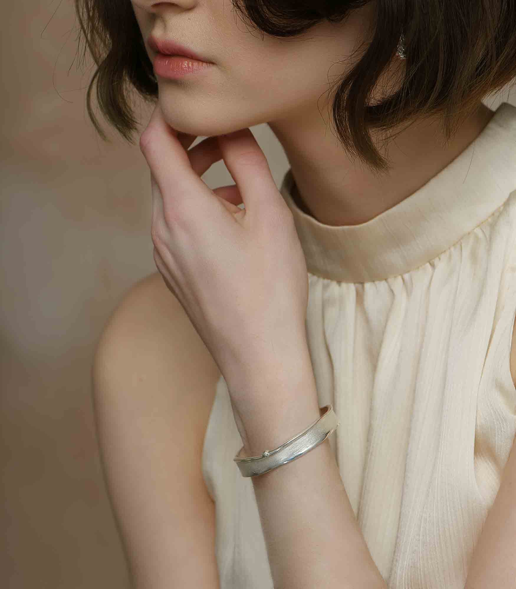 A model wearing a sterling silver bangle bracelet with a simple design featuring a brushstroke texture.