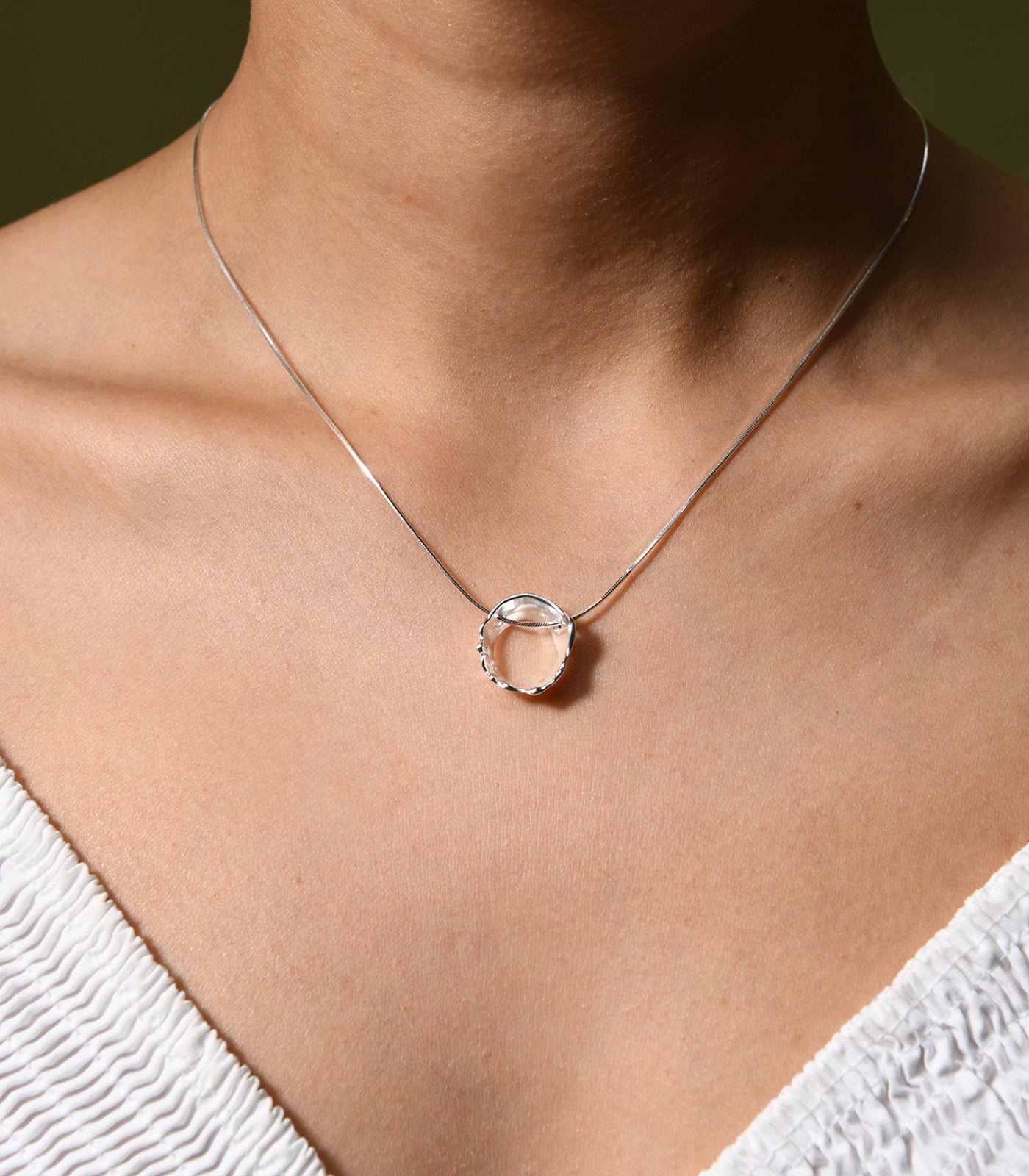 A sterling silver necklace with an irregular shaped circle pendant. The pendant is reflective of waters movements.