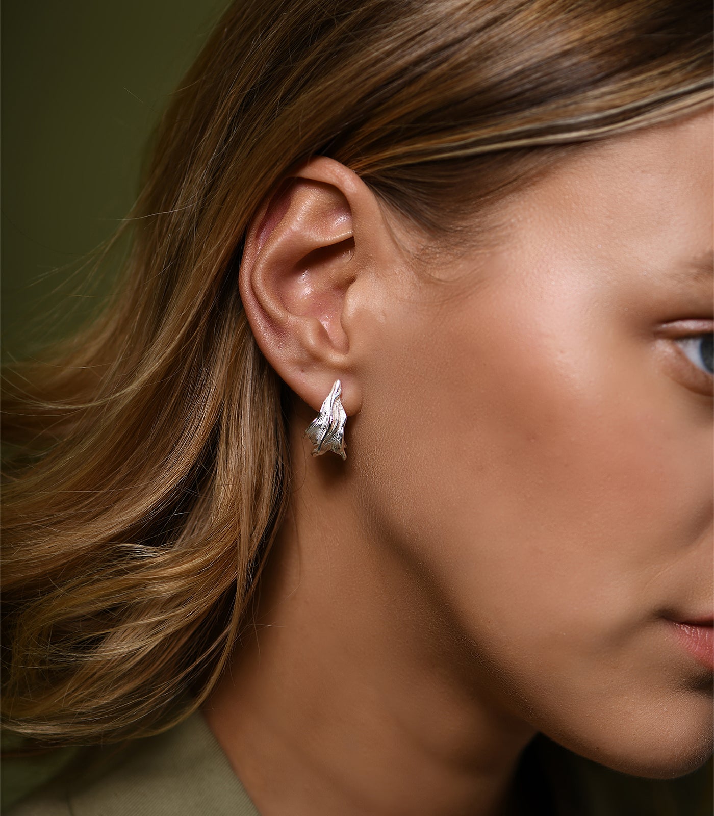 A model wears a pair of sterling silver, textured hoop earrings.