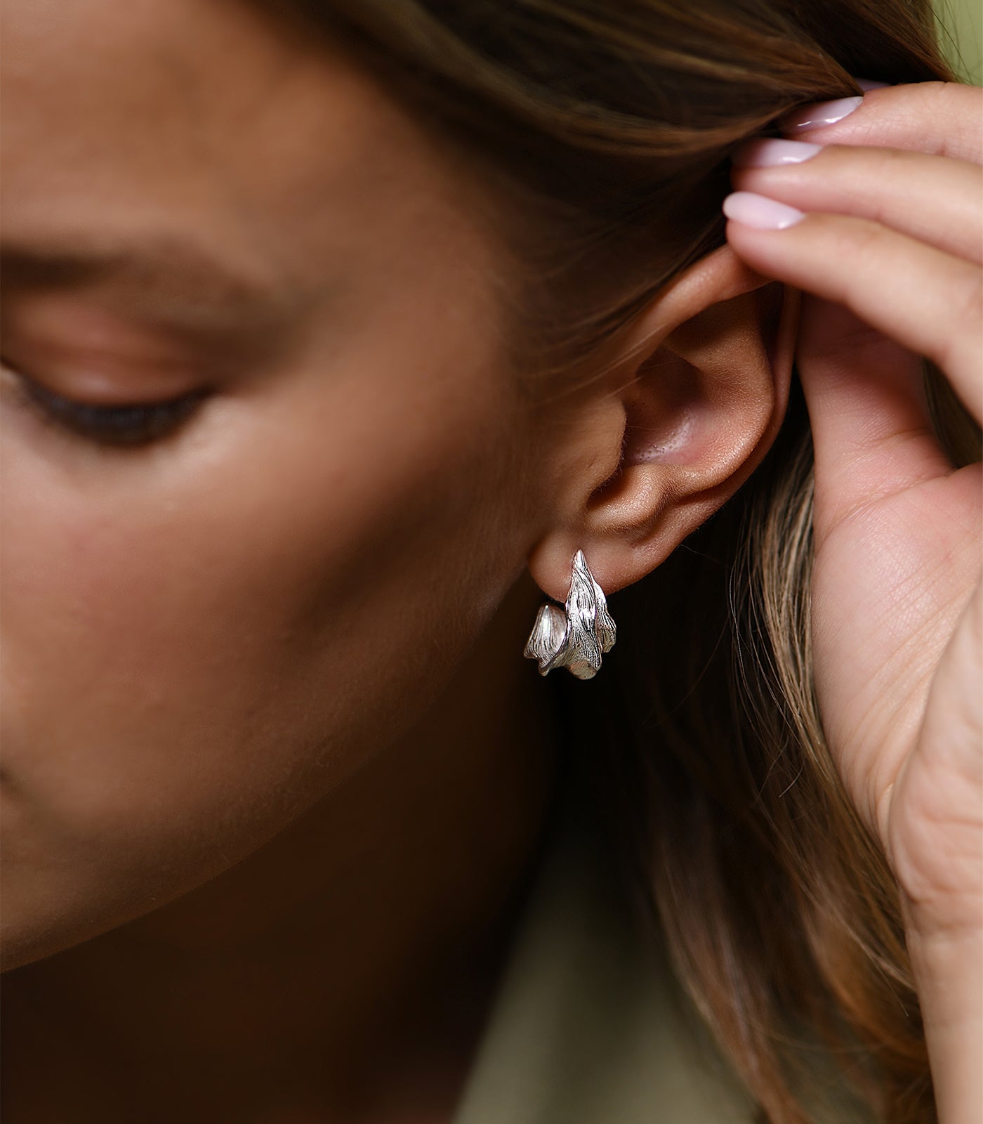 A model wears a pair of sterling silver, hoop earrings which are textured to resemble an aquatic leaf.