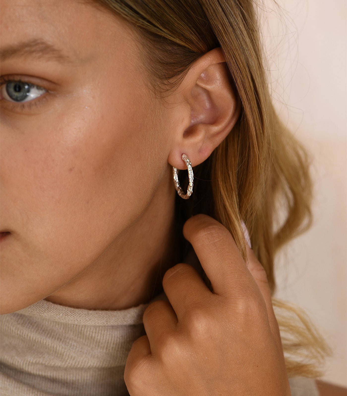 A sterling silver hoop earring. The hoop is smalll, thin and textured, creating a sophisticated design.
