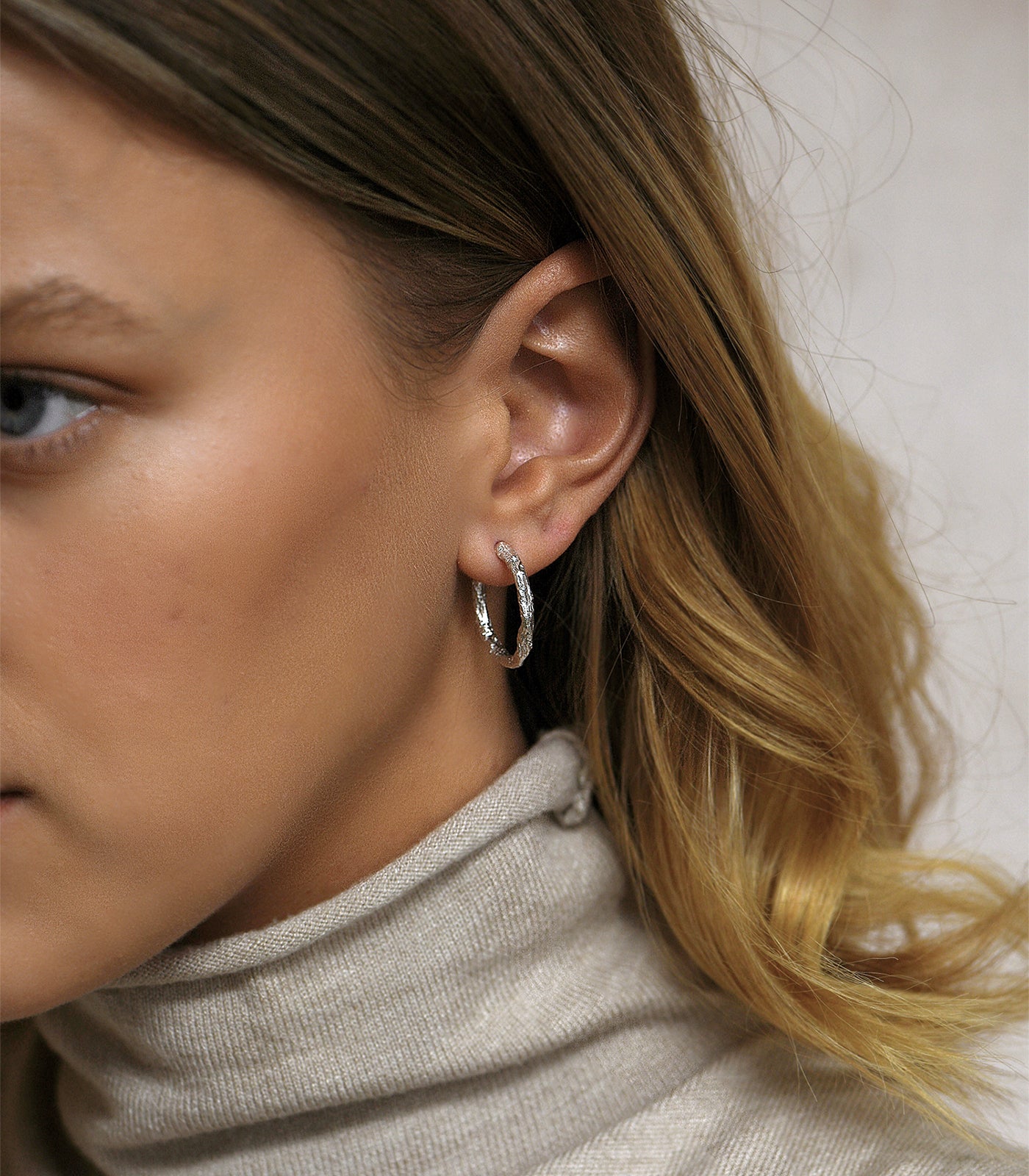 A sterling silver textured hoop earring. The hoop is small and thin, creating a sophisticated look.