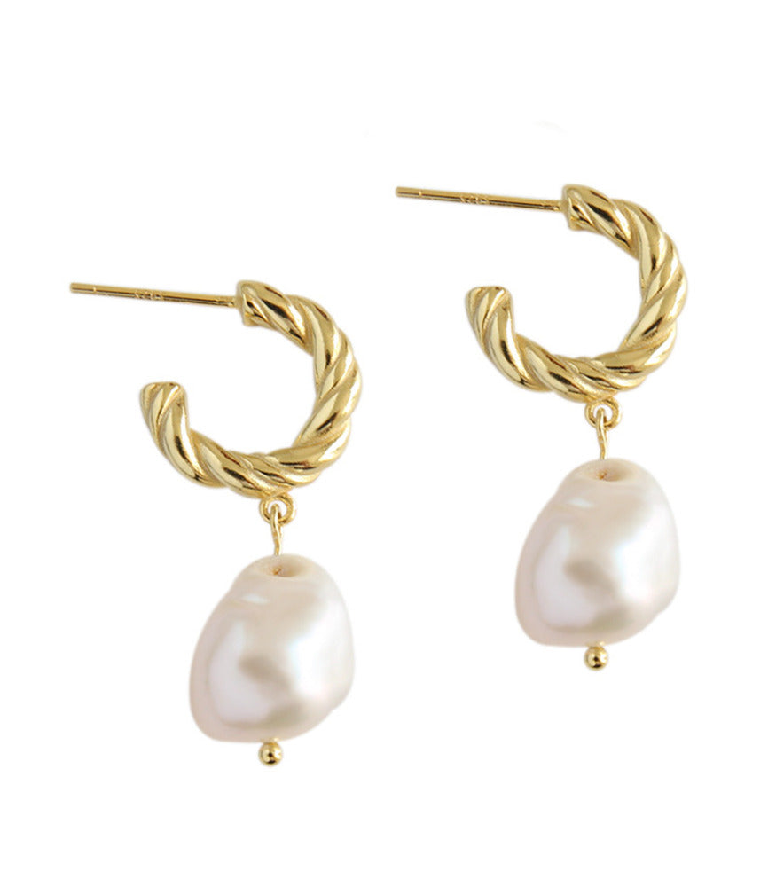 A pair of gold plated twisting hoop earrings with a baroque pearl delicately dangling from the hoops. 