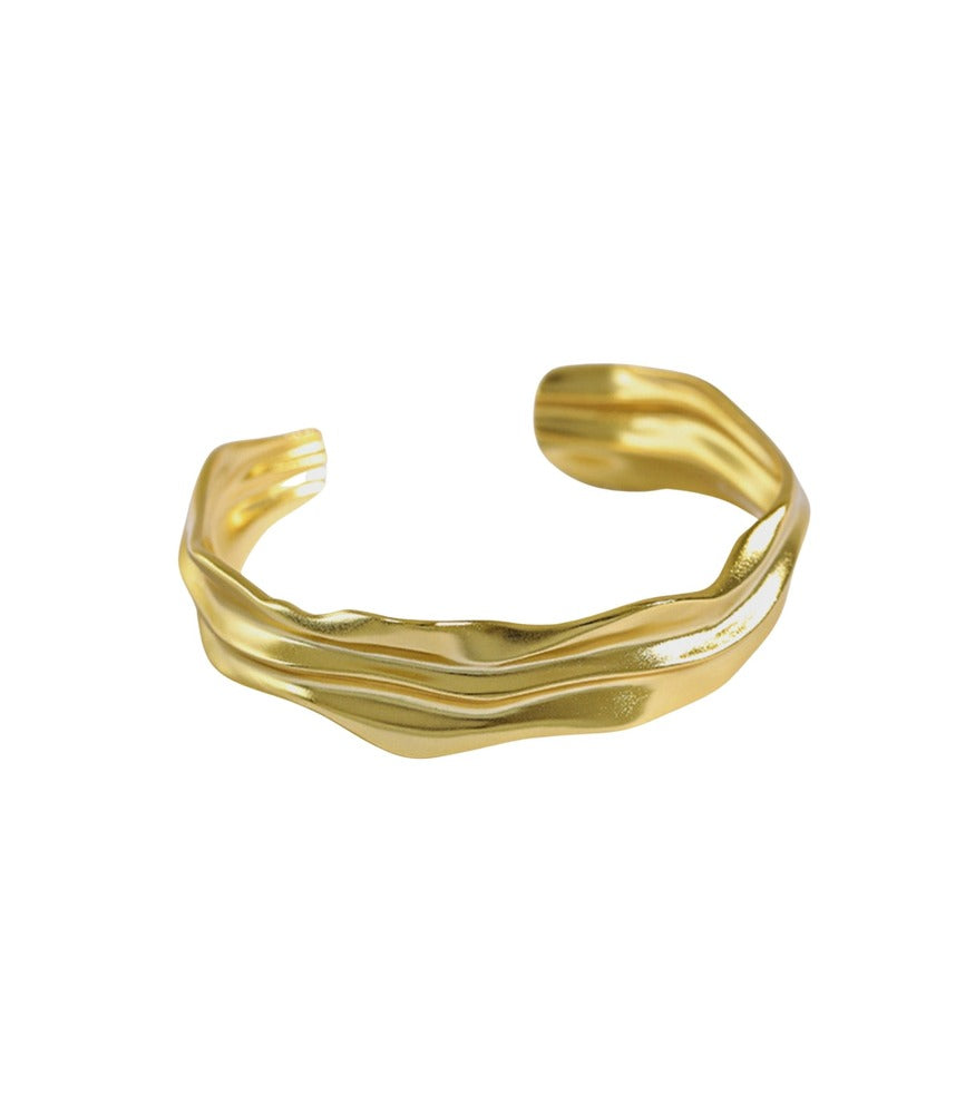 A gold plated bangle. The bangle has rigid edges with smooth flowing valleys.