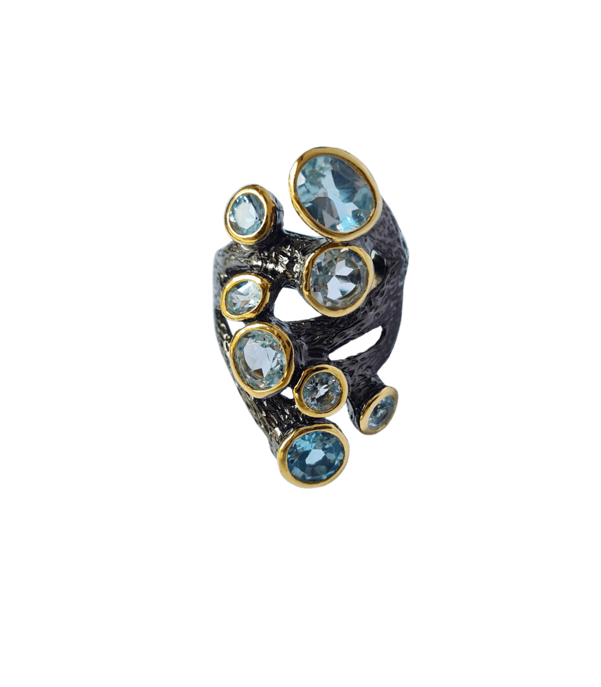 An oxidised sterling silver eyelet ring featuring an irregular shape and 8 blue topaz stones.
