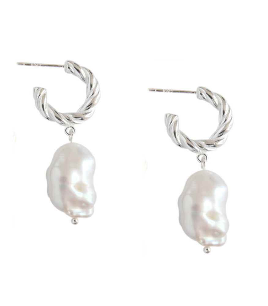 A pair of sterling silver twisting hoop earrings with a baroque pearl delicately hanging from the hoops. 