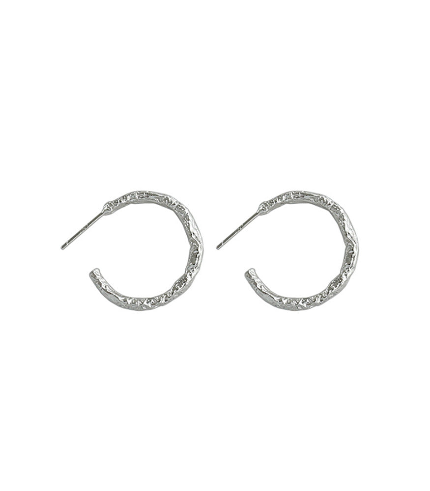 A pair of sterling silver hoop earrings. The earrings are detailed with texture, adding more dimension.