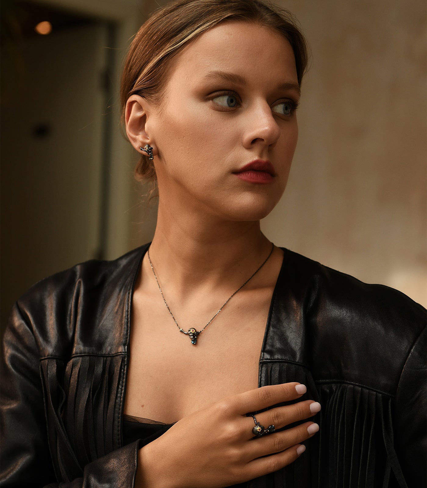 A model wears a completed set of oxidised sterling silver skull jewellery. The set includes a necklace, earrings and the ring. 