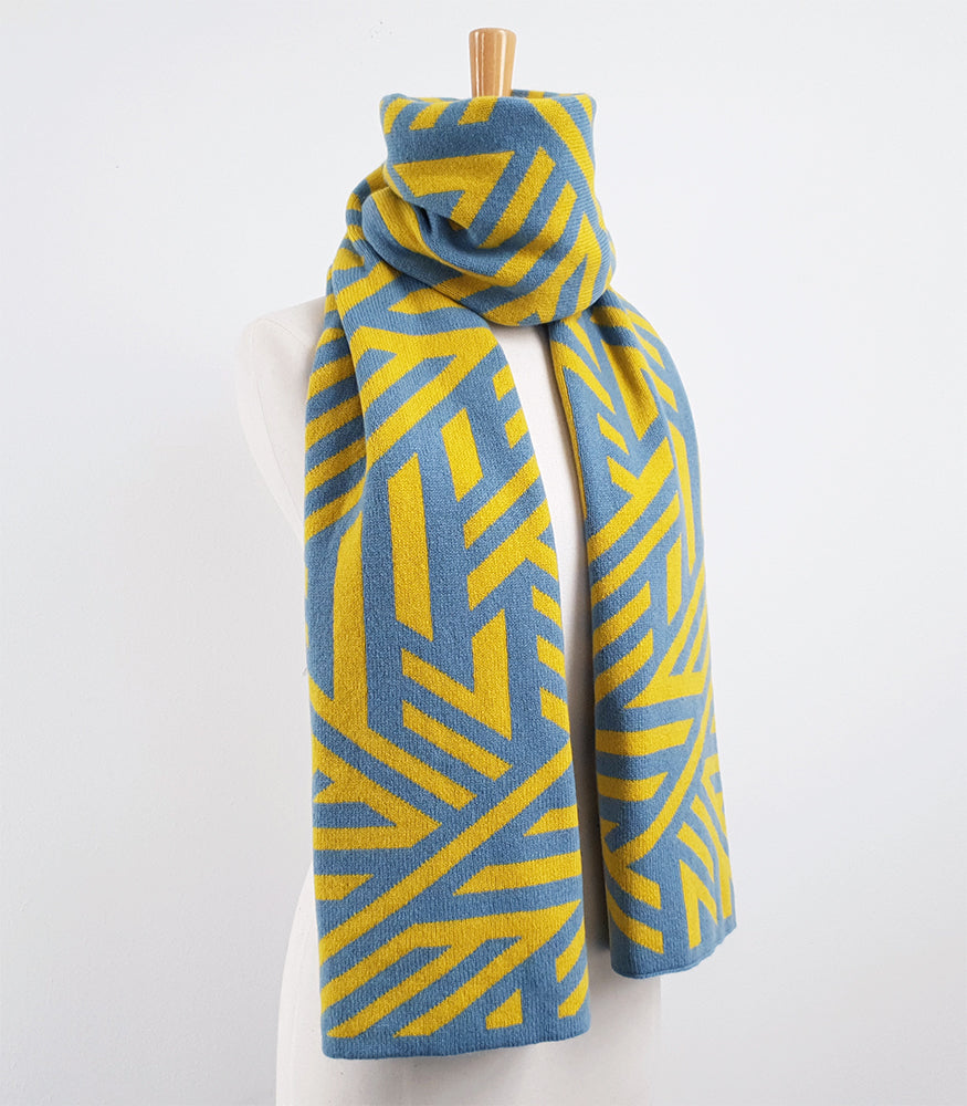 A cosy and thick yellow and blue scarf. The scarf is long and has a geometric crosswise pattern.